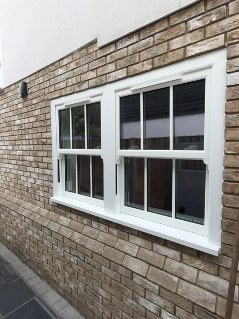 Exterior view of two white sash windows with Georgian bars fitted into a brick wall