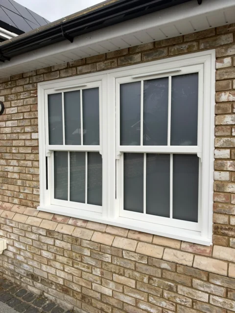 Two white sash windows with frosted privacy glass and Georgian bars beneath the roofline