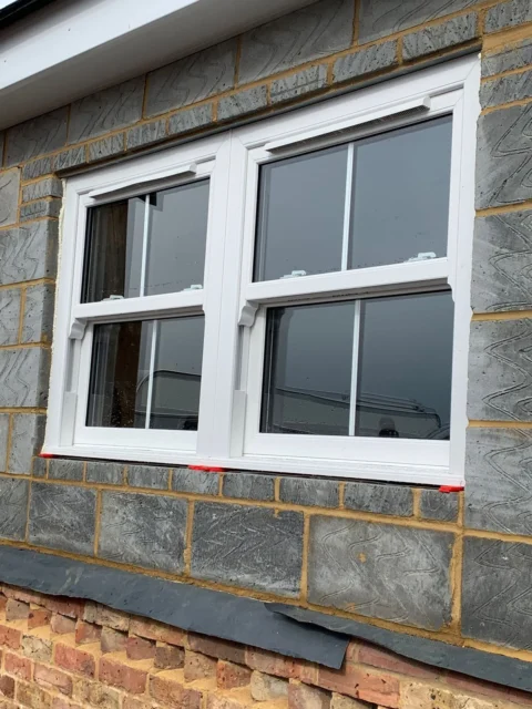 Pair of white sash windows with vertical glazing bars in a grey brick wall