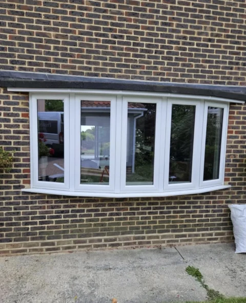 White five-panel bow window fitted in a brown brick wall