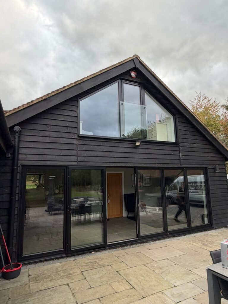 Basildon Dark-framed gable glazing and a glass Juliet balcony above wide garden doors.